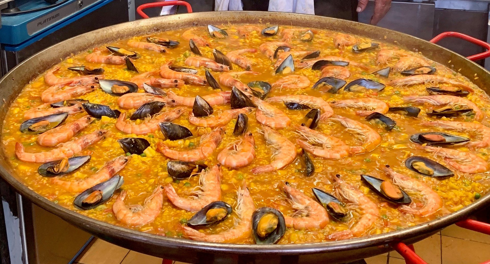 Large seafood paella in a wide shallow pan topped with shrimp and mussels in yellow saffron rice