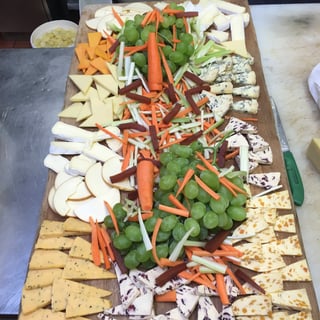 Overhead view of a charcuterie board with cheeses, crackers, fresh vegetables, and deli meats arranged on a wooden platter