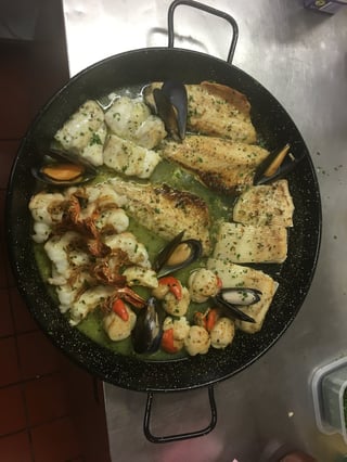 Black paella pan with seared tofu, shrimp, mussels, and vegetables in broth on stovetop