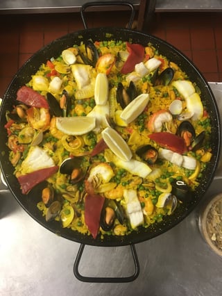 Overhead view of paella in a black speckled pan with seafood, rice, mussels, and lemon wedges